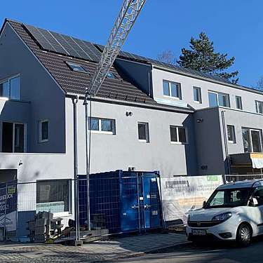 Modernes Wohnhaus mit Solarmodulen und Baustelleneinrichtung vor blauem Himmel.