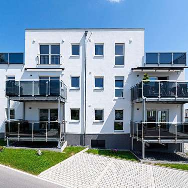 Weißes Mehrfamilienhaus mit Glasbalkonen und blauem Himmel