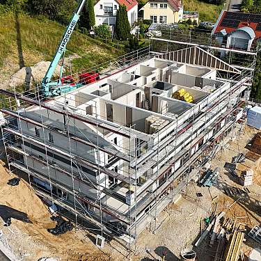 Luftaufnahme einer Hausbaustelle mit Gerüst, Kran und Rohbau in Wohngebiet.