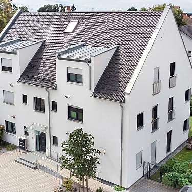 Großes weißes Wohnhaus mit Satteldach, umgeben von Garten und Nachbarhäusern.