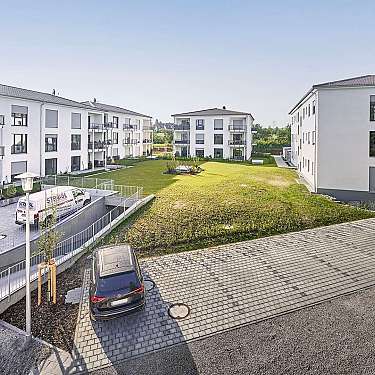 Moderne Wohngebäude umgeben einen begrünten Innenhof mit geparkten Autos.