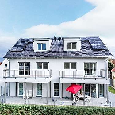 Modernes Wohnhaus mit Solarmodulen auf dem Dach und Terrasse mit rotem Sonnenschirm.