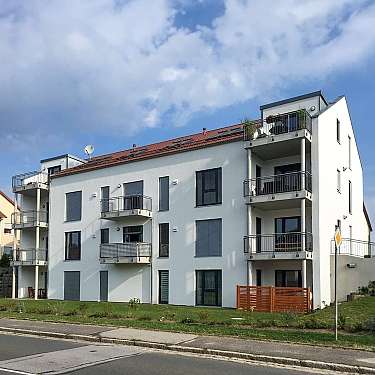 Modernes weißes Mehrfamilienhaus mit Balkonen unter blauem Himmel.
