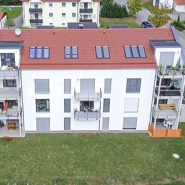 Luftaufnahme eines mehrstöckigen Wohnhauses mit rotem Dach, Balkonen und großem Garten.
