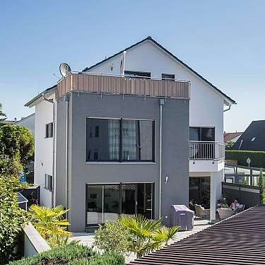 Mehrstöckiges modernes Wohnhaus mit Balkon, großen Fenstern und Garten