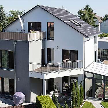 Modernes Einfamilienhaus mit Balkonen, großer Glasfront und Wintergarten im Wohngebiet.