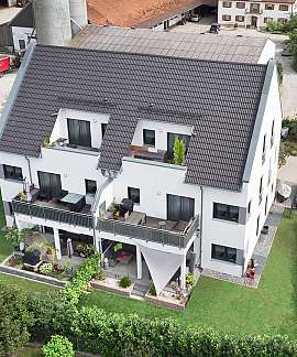Luftaufnahme eines weißen Mehrfamilienhauses mit Garten und Straße daneben.